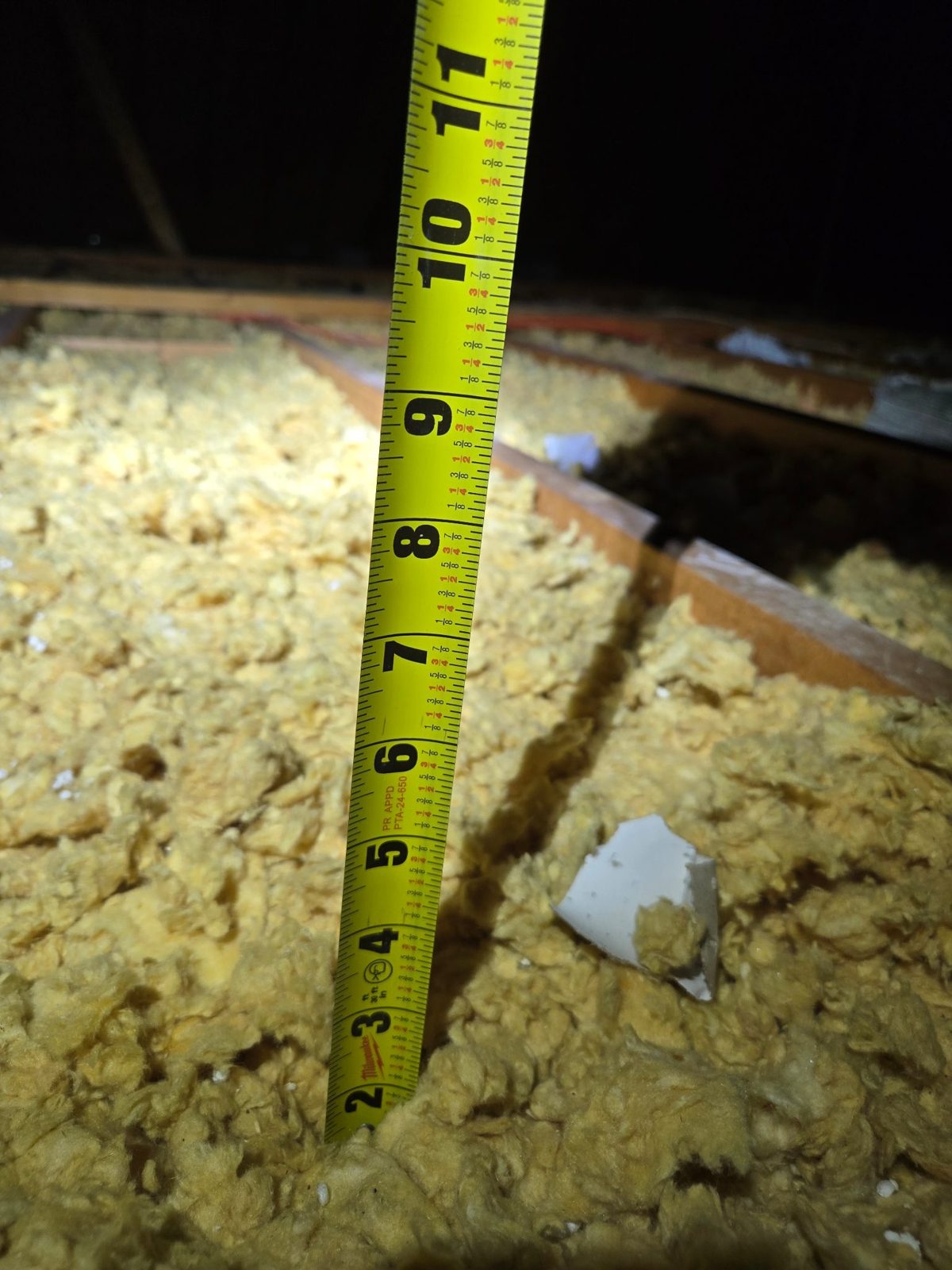 Tape measure showing barely two inches of old attic insulation before upgrade