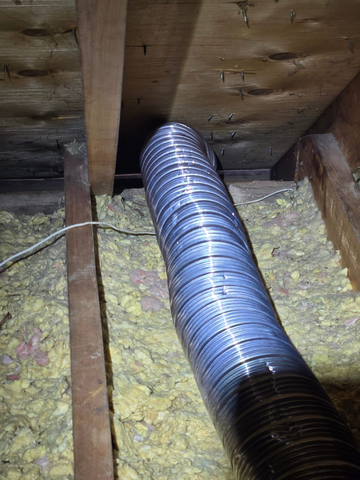 Uninsulated exhaust ducting snaking over the old insulation toward the roof deck.