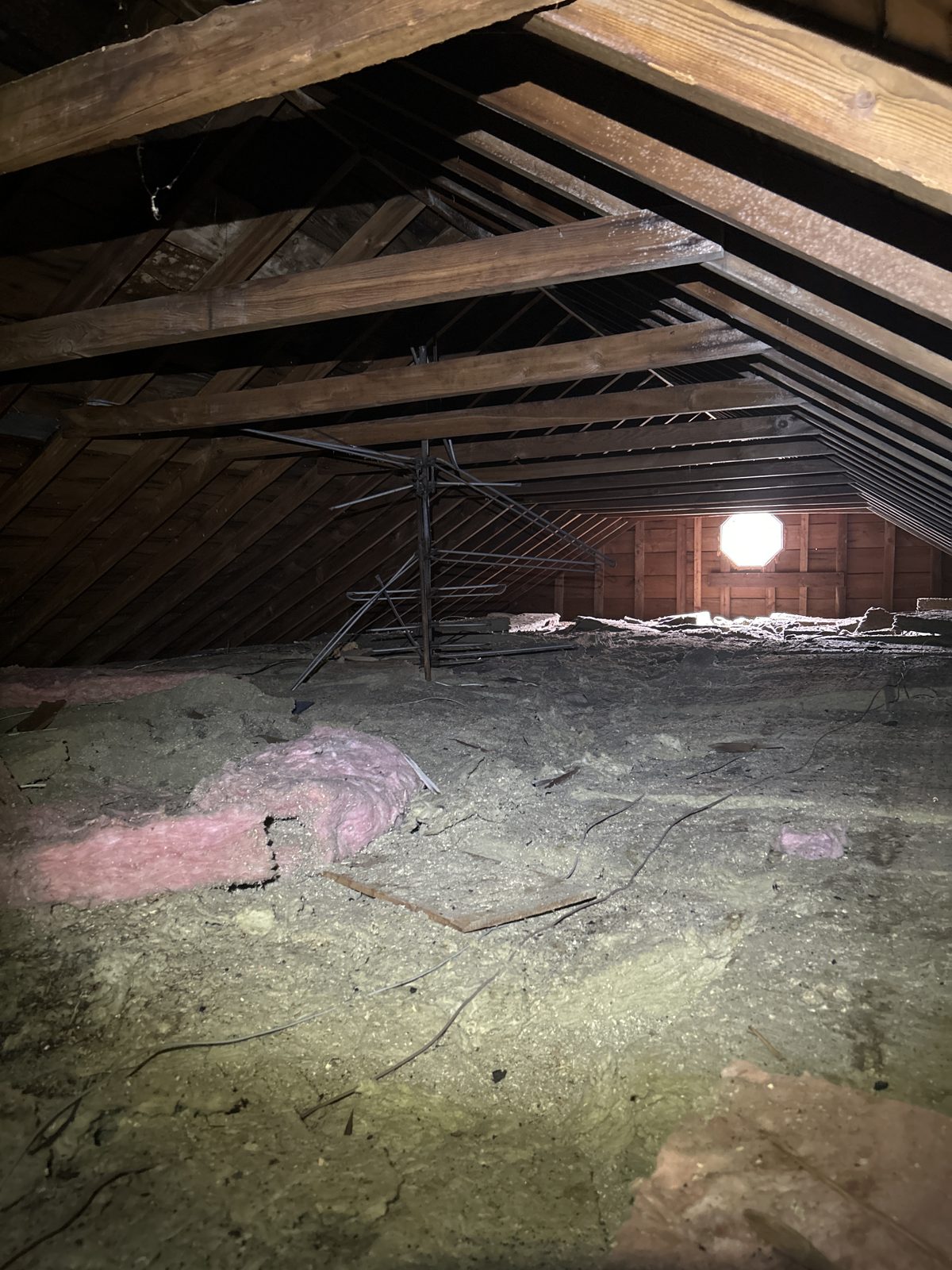 The neglected original attic: bare rafters, an old gable vent doing all the work, and decades of accumulation.